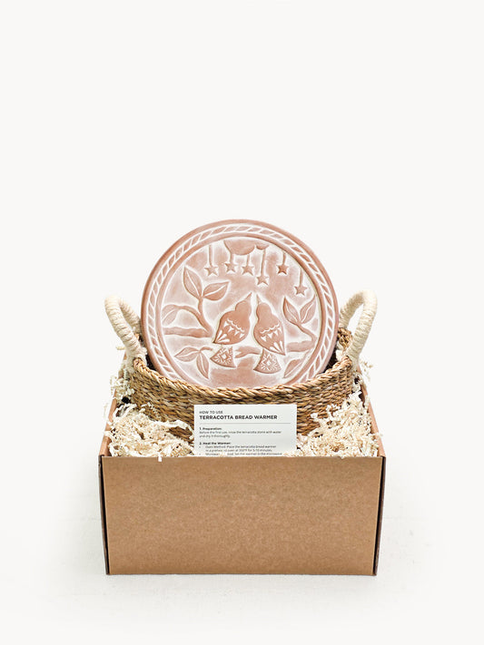 Decorative terracotta bread warmer with floral design in a cardboard box on a white background