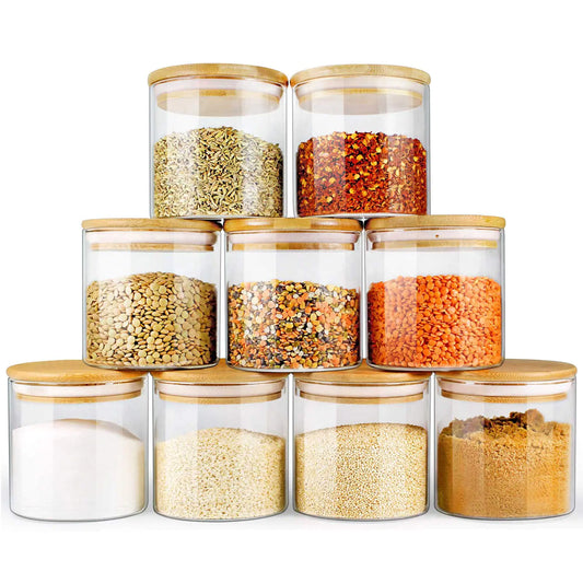 Set of glass storage jars with wooden lids containing various dry goods on a white background